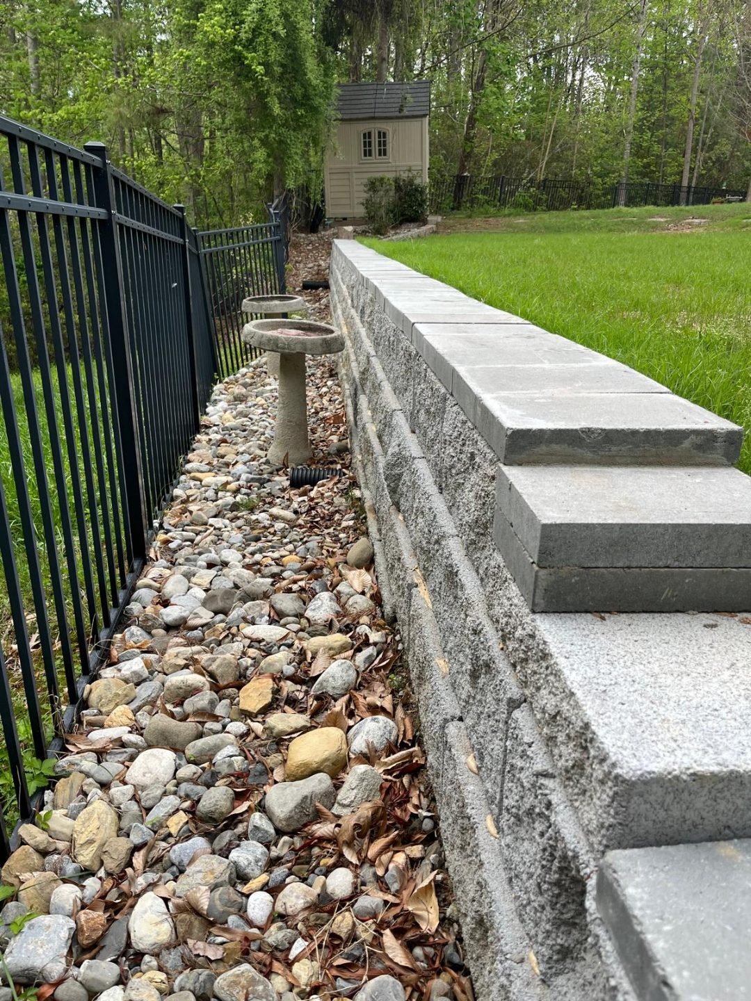 Capped block retaining wall with river-rock drainage bed and aluminum fence
