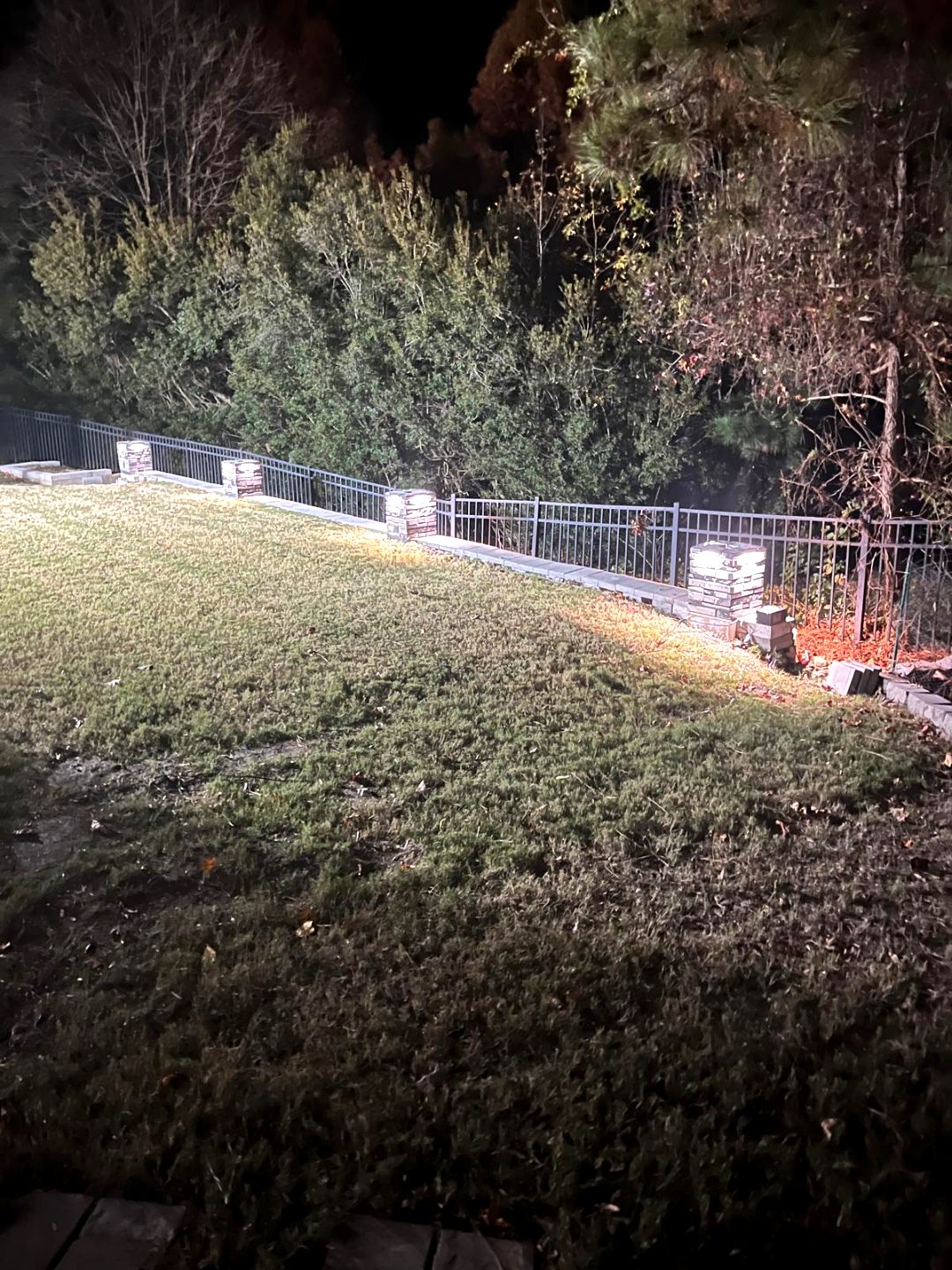 Lit stone column caps along a fence line at night